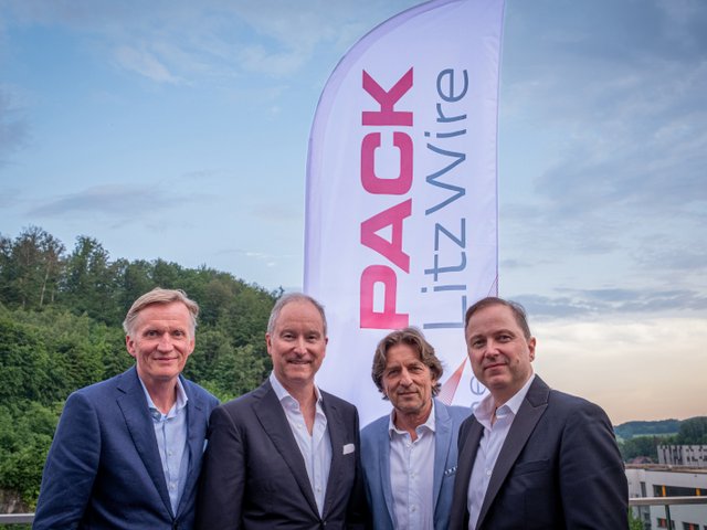 Vier Männer stehen nebeneinander vor einer Fahne mit der Aufschrift „PACK LitzWire“