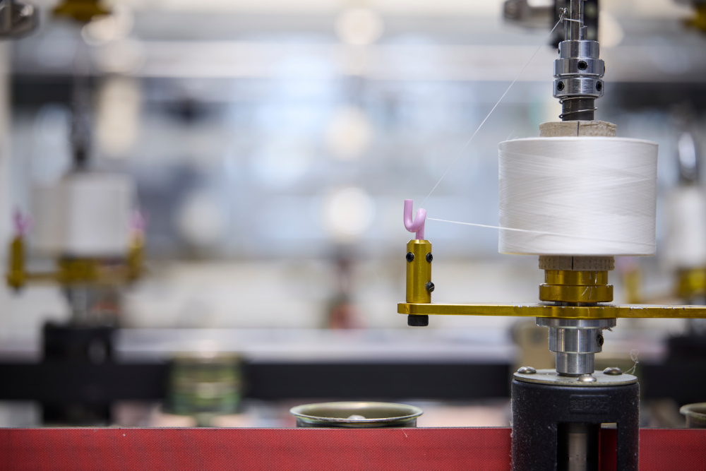 Spule mit weißem Faden an einer Produktionsmaschine während eines Veredelungsprozesses.
