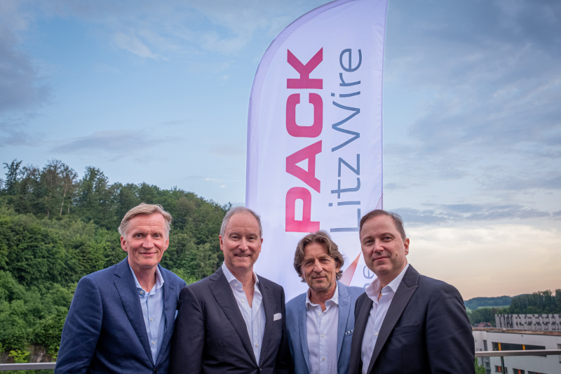 Vier Männer stehen nebeneinander vor einer Fahne mit der Aufschrift „PACK LitzWire“